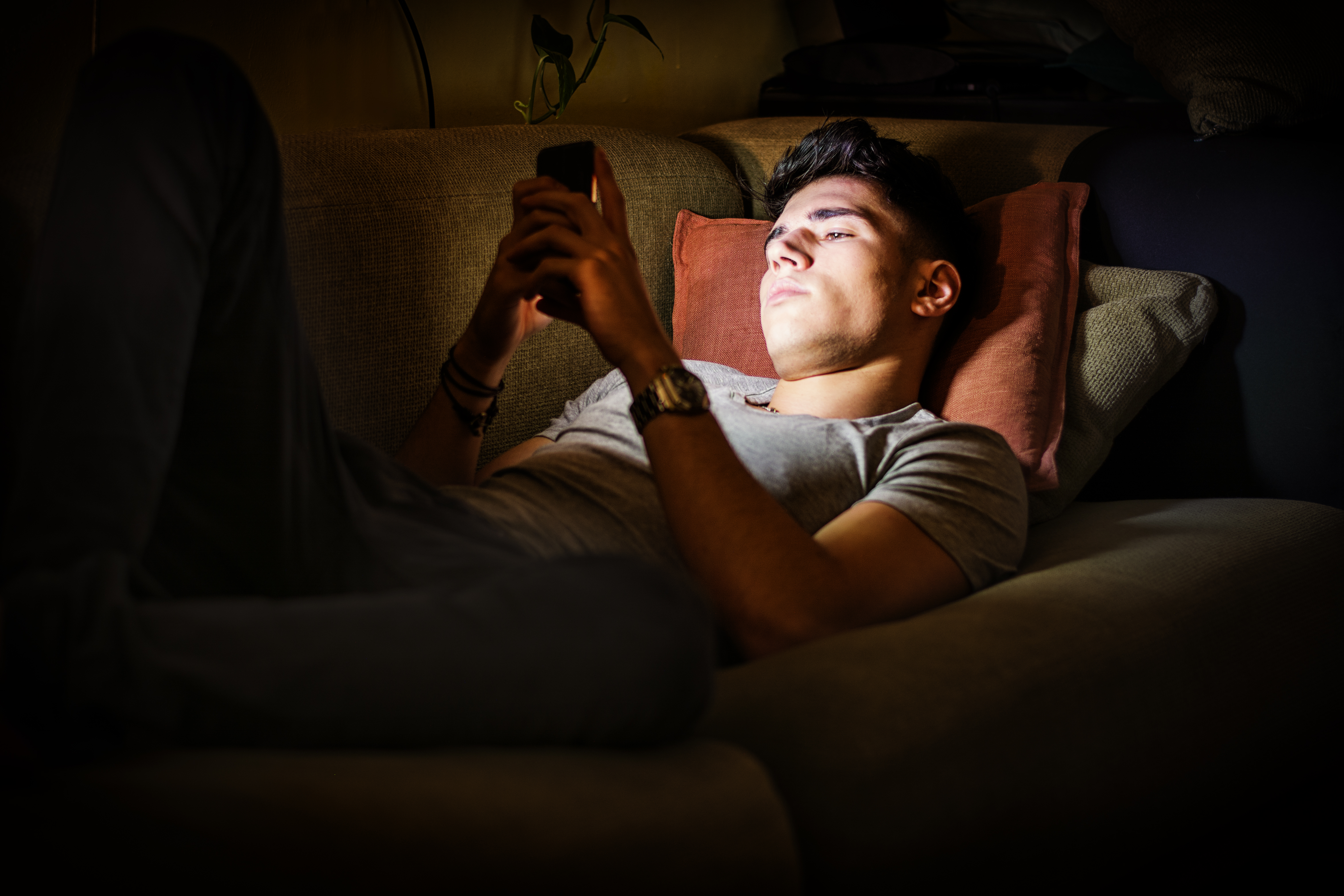 Young Man on Sofa Lit by Light from Cell Phone