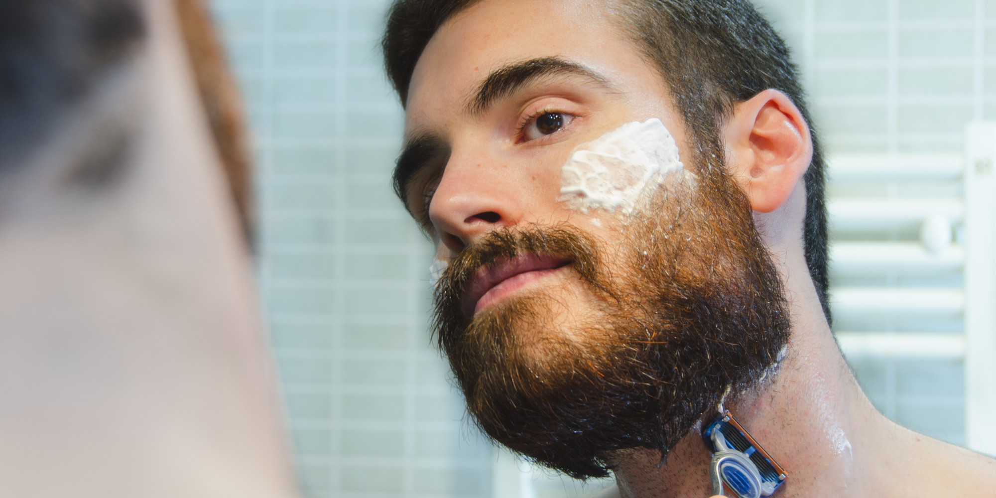 Man in the bathroom caring for his beard with a razor and shaving foam