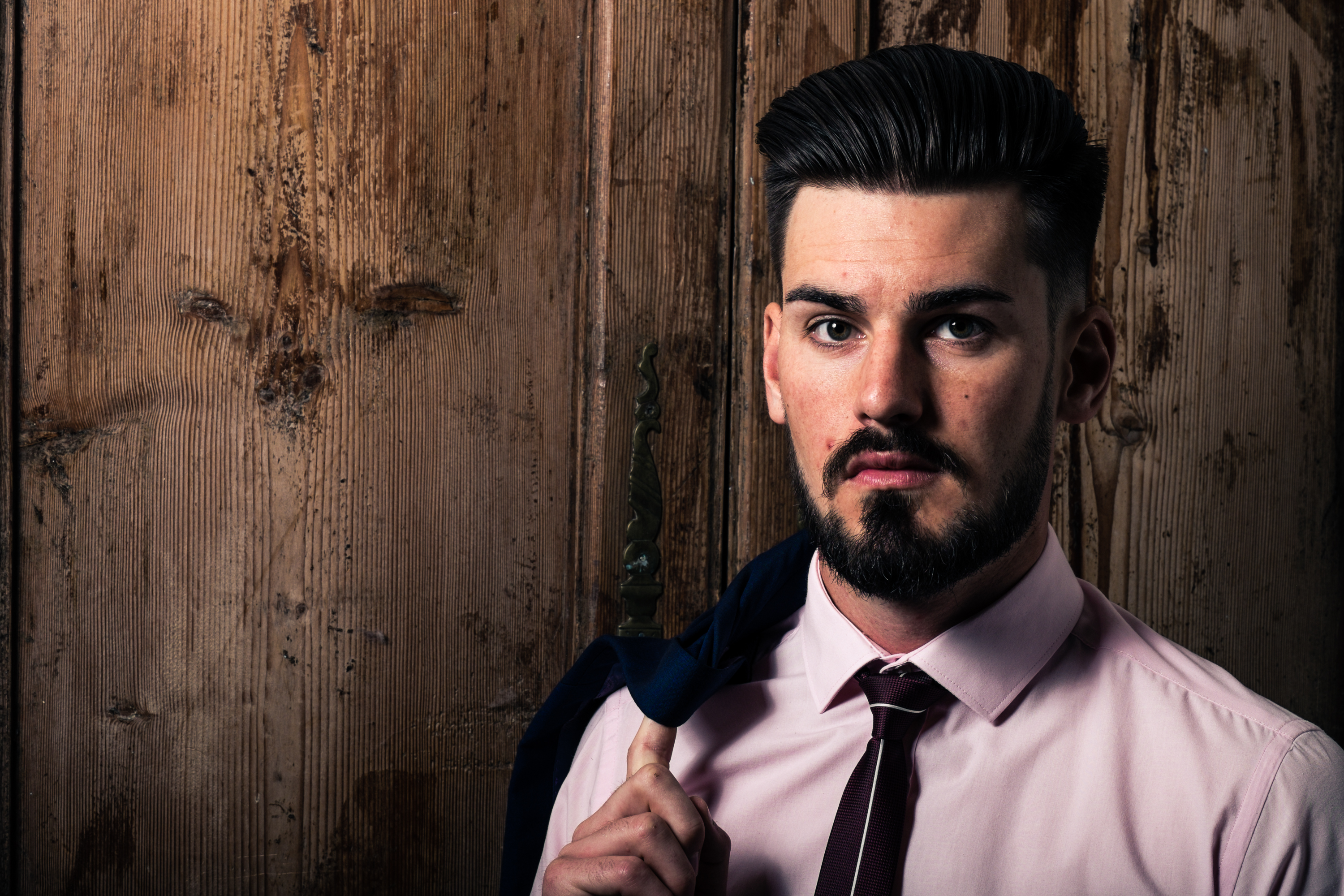 Very smart young man with blazer over his shoulder in front of wood background