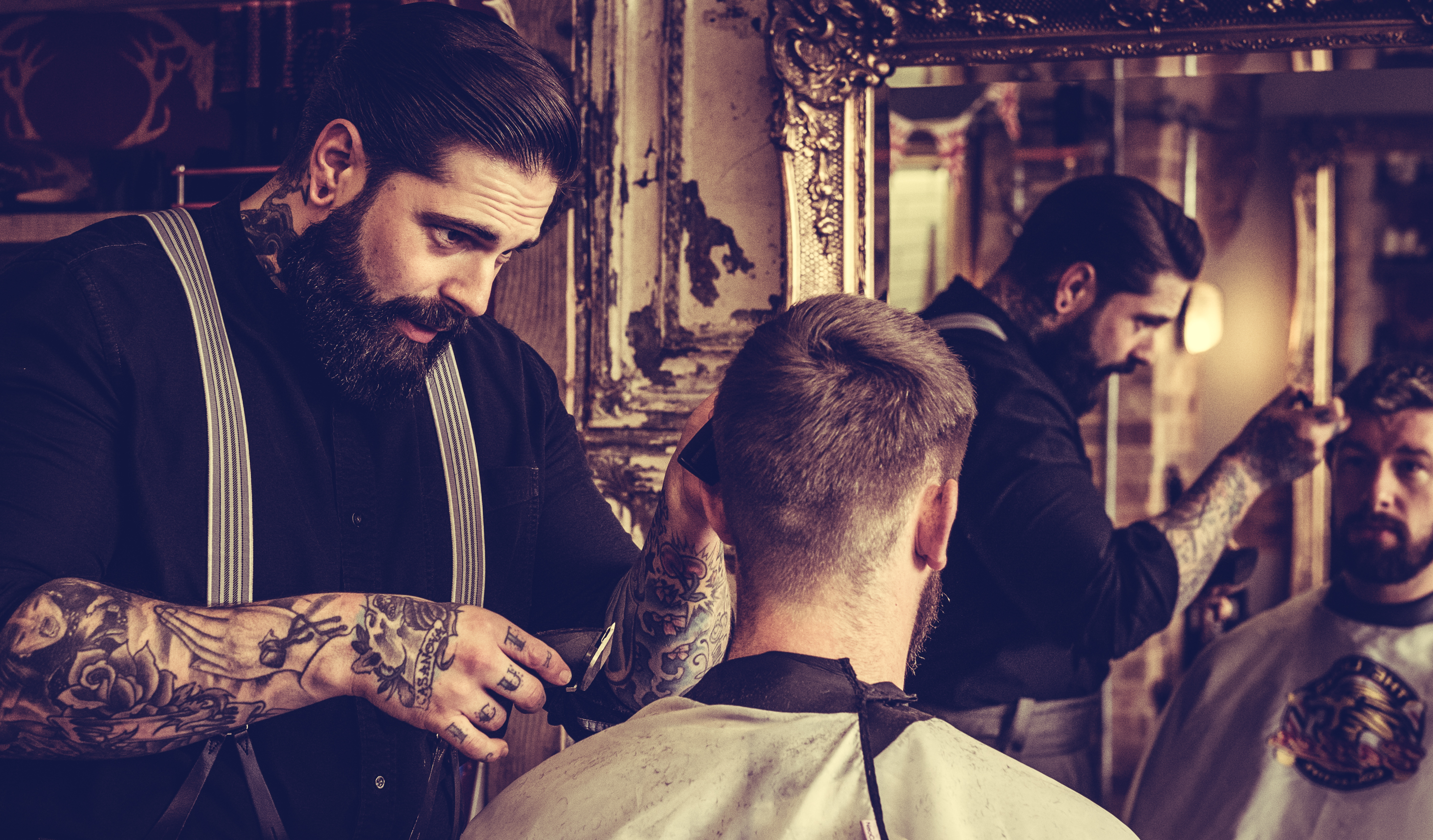 Man having hair cut in the barbers chair by barber man who has tattoos