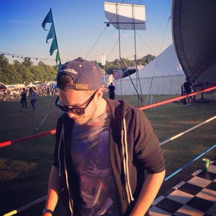 Man at a festival wearing sunglasses and a snapback with blue sky and music