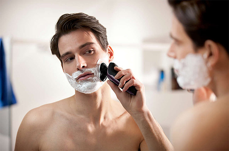 Man shaving face in the mirror with electric razor