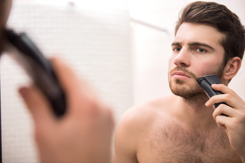 Man shaving face in the mirror with electric razor