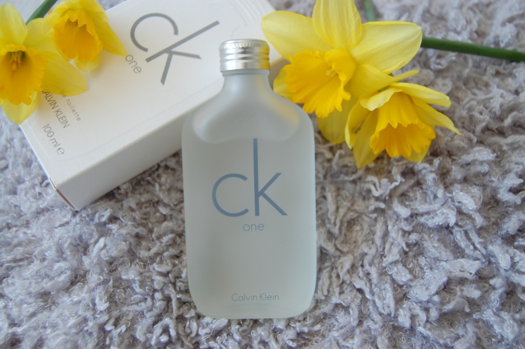 Calvin Klein CK One Eau de Toilette perfume bottle lay on a fluffy cushion with yellow daffodil flowers for mother's day